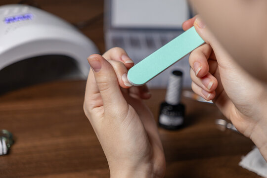 Woman shaping her natural nails meticulously with a mint-green nail file, performing a detailed DIY self-manicure at home, promoting beauty, hygiene, and personal pampering