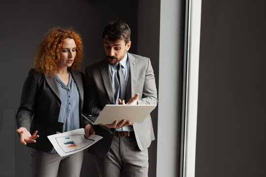 Businessman and businesswoman working together in a modern office, analyzing business data on a laptop.

