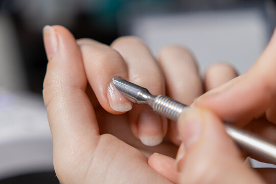 Woman performing self-manicure, meticulously pushing back cuticles on natural fingernails using a metal tool for essential personal nail care and beauty
