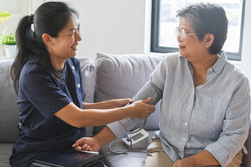 Pressure measurement of hypertension in elderly woman sitting on couch, young woman nurse or...