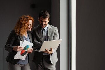 Businessman and businesswoman working together in a modern office, analyzing business data on a laptop.