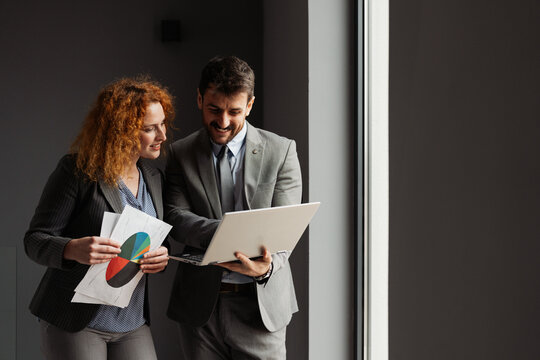 Businessman and businesswoman working together in a modern office, analyzing business data on a laptop.

