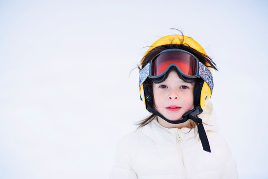 Close-up of Portrait of a young girl with freckles standing in a snowy landscape wearing a skiing helmet and ski goggles