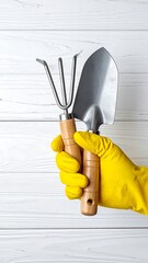 A gloved hand holding garden tools against a white wooden background