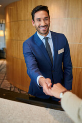 Fototapeta premium Smiling hotel receptionist greeting a guest with a handshake at the front desk