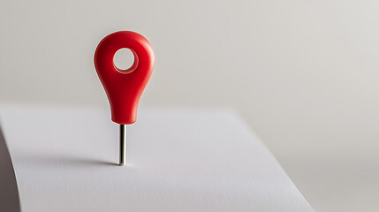 A red pin stands vertically on a white surface, casting a subtle shadow. The simplicity of the composition draws attention to the pin's bold color and clean design, highlighting location.