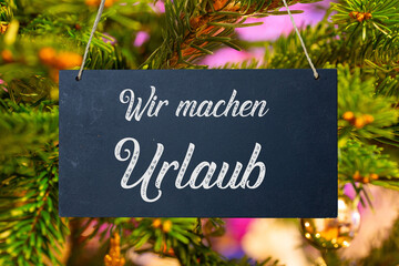 Betriebsferien an Weihnachten: Schild mit der Aufschrift WIR MACHEN URLAUB vor einem Weihnachtsbaum