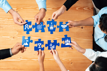 Diverse group of people collaborating around a wooden table, connecting puzzle pieces that symbolize teamwork and various concepts of achievement and partnership. Amity
