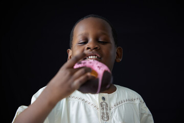 African boy eating chocolate glazed donut on black background