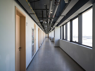 Long office corridor with exposed pipes, windows, and doors