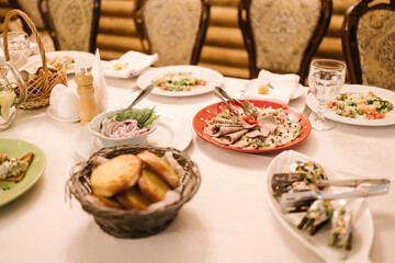 Elegant dining table set with Russian-style dishes: sliced meat, fresh salads, pickled onions, bread basket, garnishes, and glassware. Luxurious chairs and warm lighting create a refined atmosphere