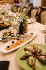 Elegant banquet table with gourmet appetizers: smoked salmon slices, cucumber rolls, open-faced sandwiches with cream topping. Delicate floral arrangement and crystal glasses add sophistication — idea