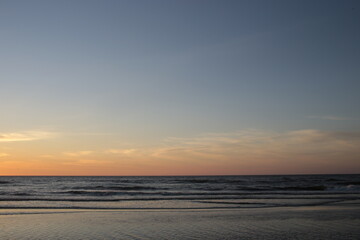 Fototapeta premium A minimalist view of a vast, clear blue-to-orange twilight sky over the dark, calm ocean and beach.