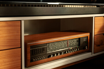 Vintage wooden radio receiver in mid-century modern cabinet under warm sunlight, retro interior detail with nostalgic atmosphere.