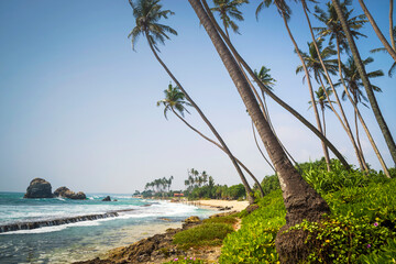 Topical beach with traditional fishing stilts in the distance on Koggala beach, Galle, Southern Province, Sri Lanka