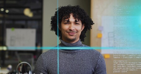 Smiling developer wearing grey sweater at office cubicle, with computer monitor and code overlay