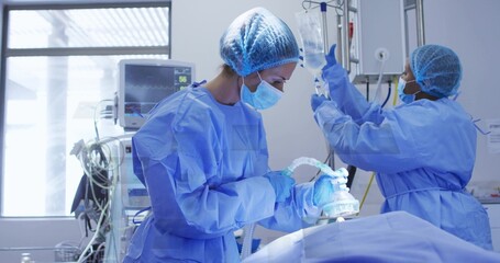 Operating surgeon holding anesthesia mask over patient in OR, with assistant adjusting IV fluid bag