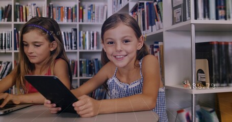 Studying two girls in blue sleeveless dress, red top at library, with tablet laptop grid table © vectorfusionart