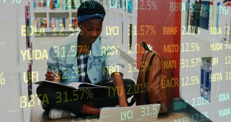 Writing student referencing laptop, notebook and pen in library aisle, with financial data overlay