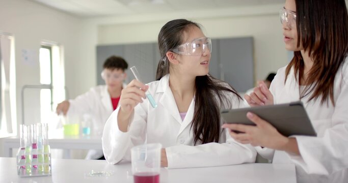 Analyzing blue solution Chinese girl wearing lab coat and goggles holding test tube in laboratory