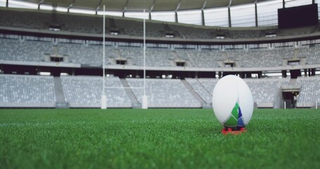 Resting rugby ball on orange kicking tee at stadium with goalposts and scoreboard, copy space