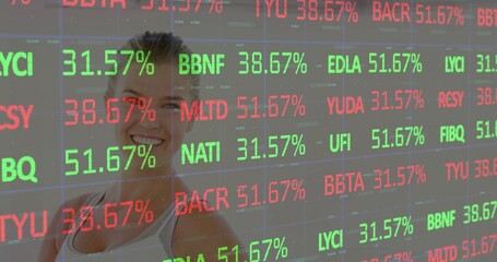 Smiling woman standing behind transparent display at trading floor, displaying tickers in red green