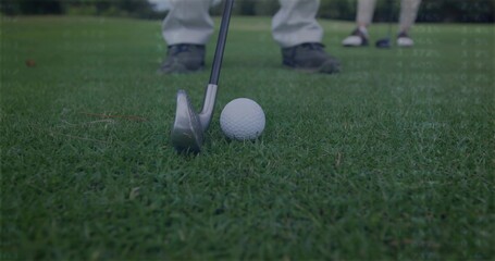 Aligning instructor adjusting iron club behind golf ball on tee at fairway, with student watching