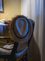 Straw hat hanging on a rattan chair in soft blue light. Vintage workspace.