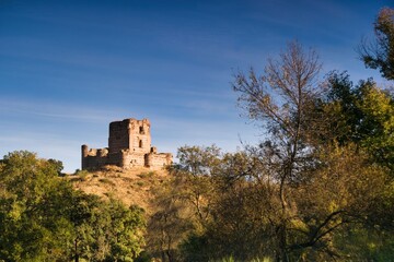 Ruined castle on a hill surrounded by trees under a bright blue sky