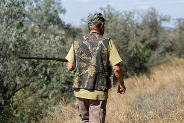 A hunter with a gun in camouflage clothing. A gentleman with a gun, medium shot, unrecognizable.