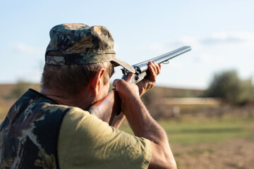 An adult hunter hunts in the autumn countryside. He fires a shotgun.