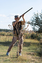 An adult hunter hunts in the autumn countryside. He fires a shotgun.