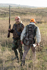 A hunters in camouflage clothing with a gun in his hands walks along the reeds.
