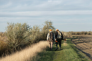 A hunters in camouflage clothing with a gun in his hands walks along the reeds.