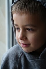Young boy in a gray hoodie gazing thoughtfully out the window