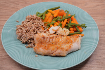 Delicious baked cod fillet with vegetables and buckwheat on a blue plate