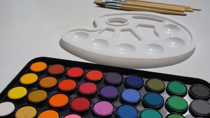 Watercolor paints, brushes and a sheet of paper on a white background