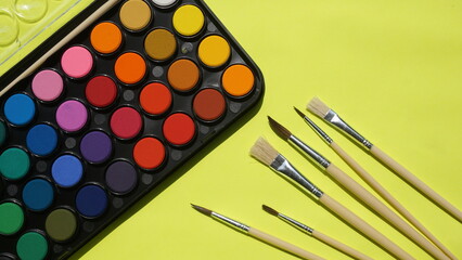 Set of watercolor paints and brushes on a light green background