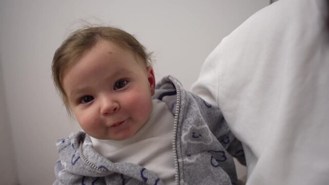 Smiling baby looking up while being held in arms, joyful infant expression showing comfort and affection, tender family moment of warmth and connection at home