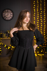 A woman in a black dress and stockings stands in front of a Christmas tree. She smiles and poses for the camera. The concept of holidays and Christmas.
