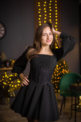 A woman in a black dress and stockings stands in front of a Christmas tree. She smiles and poses for the camera. The concept of holidays and Christmas.