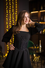 A woman in a black dress and stockings stands in front of a Christmas tree. She smiles and poses for the camera. The concept of holidays and Christmas.