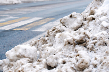 Melting slush accumulation on crosswalk area, winter thaw and municipal cleaning results. Road residue and dirty snow piles after plowing operations, municipal cleanup aftermath