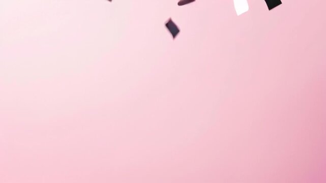 A loop video of colorful silver confetti gently falling over a flat pink background, creating a calm and cheerful atmosphere.