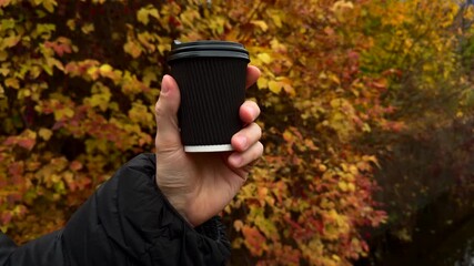 A black glass with a hot drink on the tipple against the background of yellow autumn trees.