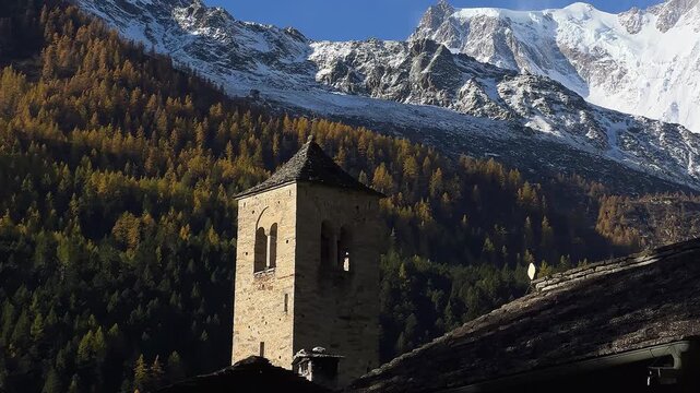 Macugnaga, Italy. Old stone bell tower with a mountain and glacier in the background in autumn. European Alps with Monte Rosa. Famous summer and winter tourist destination. Pan and tilt