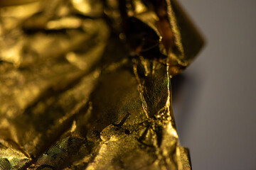 A detailed macro photo of a golden-colored shining chocolate wrapper, capturing texture, light reflection, and luxurious appeal.