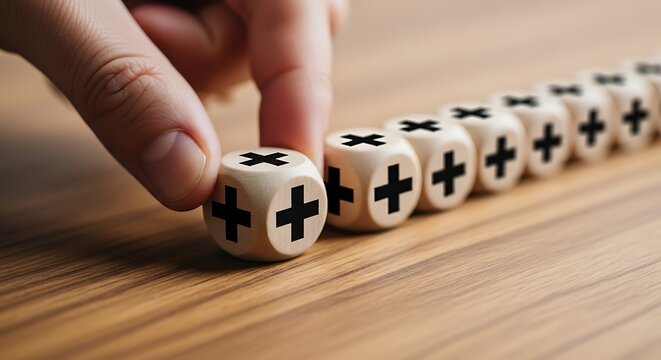 Hand placing wooden dice with plus signs in a row on a table