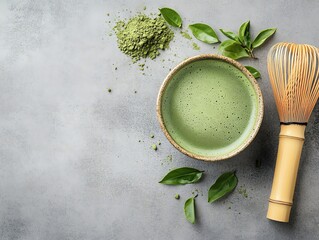 Matcha tea in a bowl, with froth, alongside a bamboo whisk and powder, on a gray background, top view, copy space