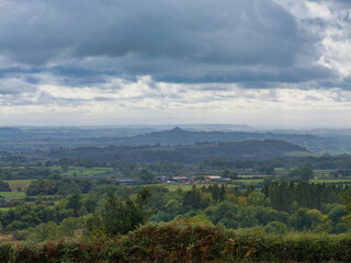 View across the Somerset Levels to Glastonbury Tor and St Michaels Tower on an overcast afternoon in Somerset, UK. Moody clouds and layered green farmland.